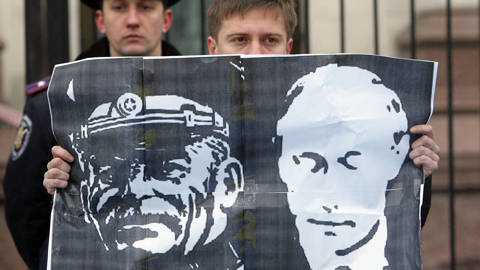 Protestor holds a flag with Stalin and Putin on it.