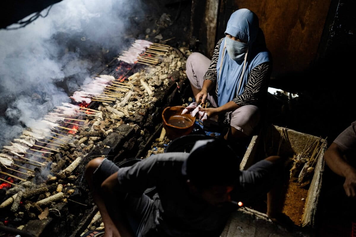 Women grill skewered shark meat at a warehouse in Rumbuk village
