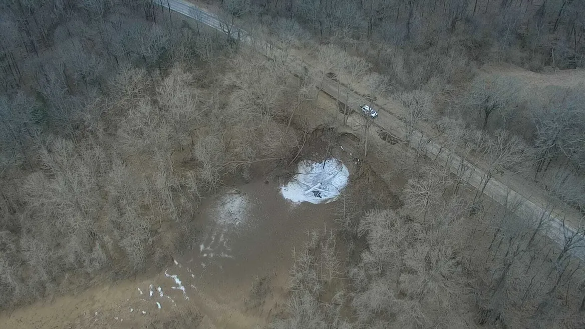 Overhead shot of a bleak roadway and barren trees with a white crater