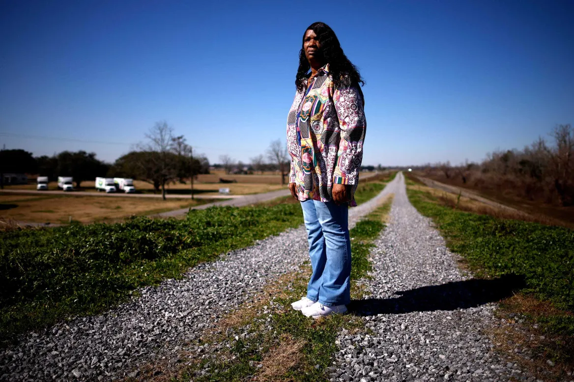 Woman in a colorful-print top, blue jeans, and white sneakers standing on gravel tracks