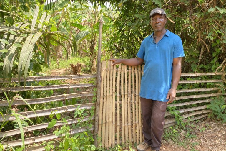 James Kwegyir Ampah, an elder of the village of Krofu, neighboring Krampakrom, stands outside the fence. His land has been split in half by the mine’s boundary line. Image by Maxine Betteridge-Moes for Mongabay.