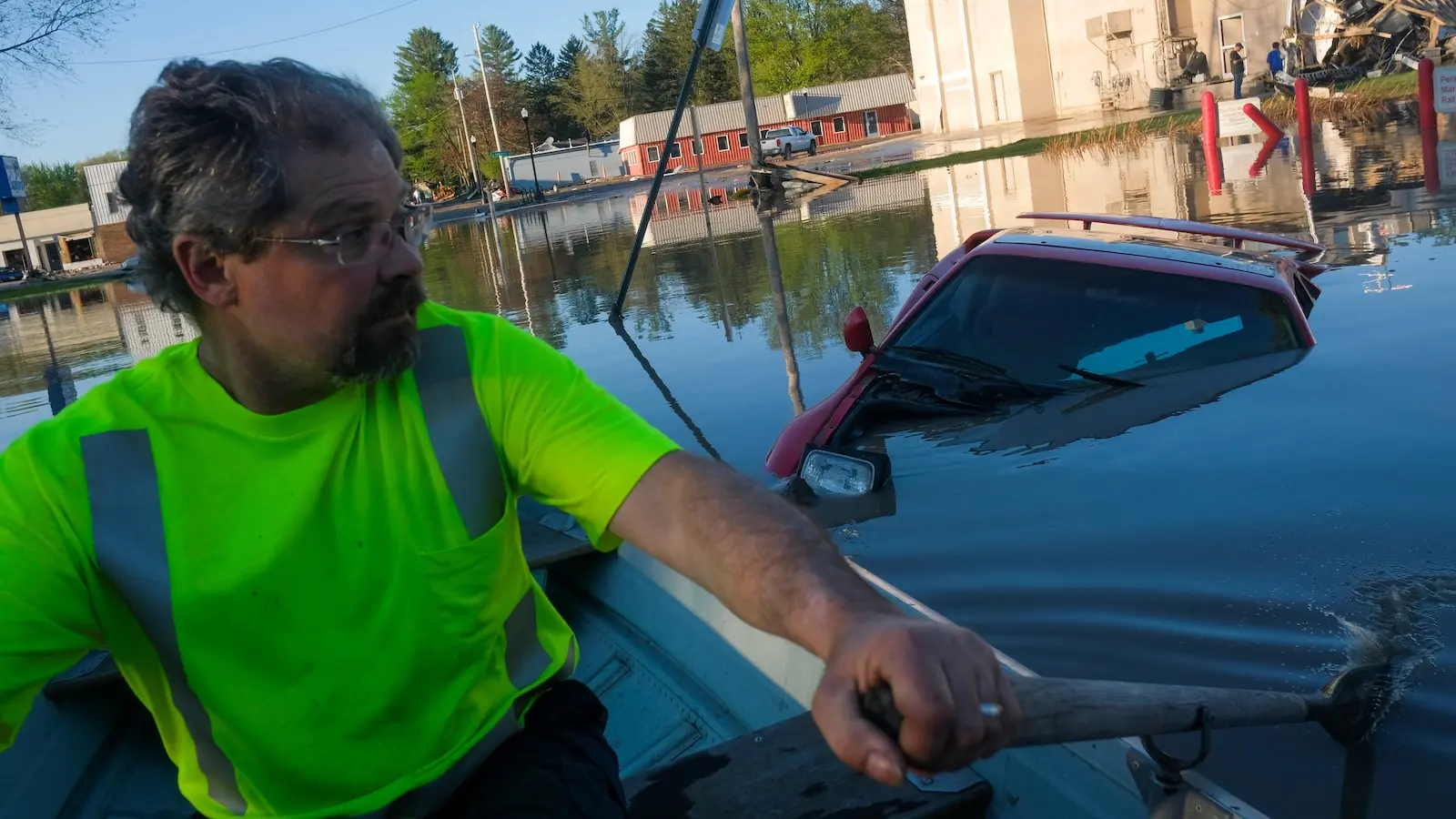A man in a rowboat passes a submerged car in the flooded streets of Sanford, Michigan.