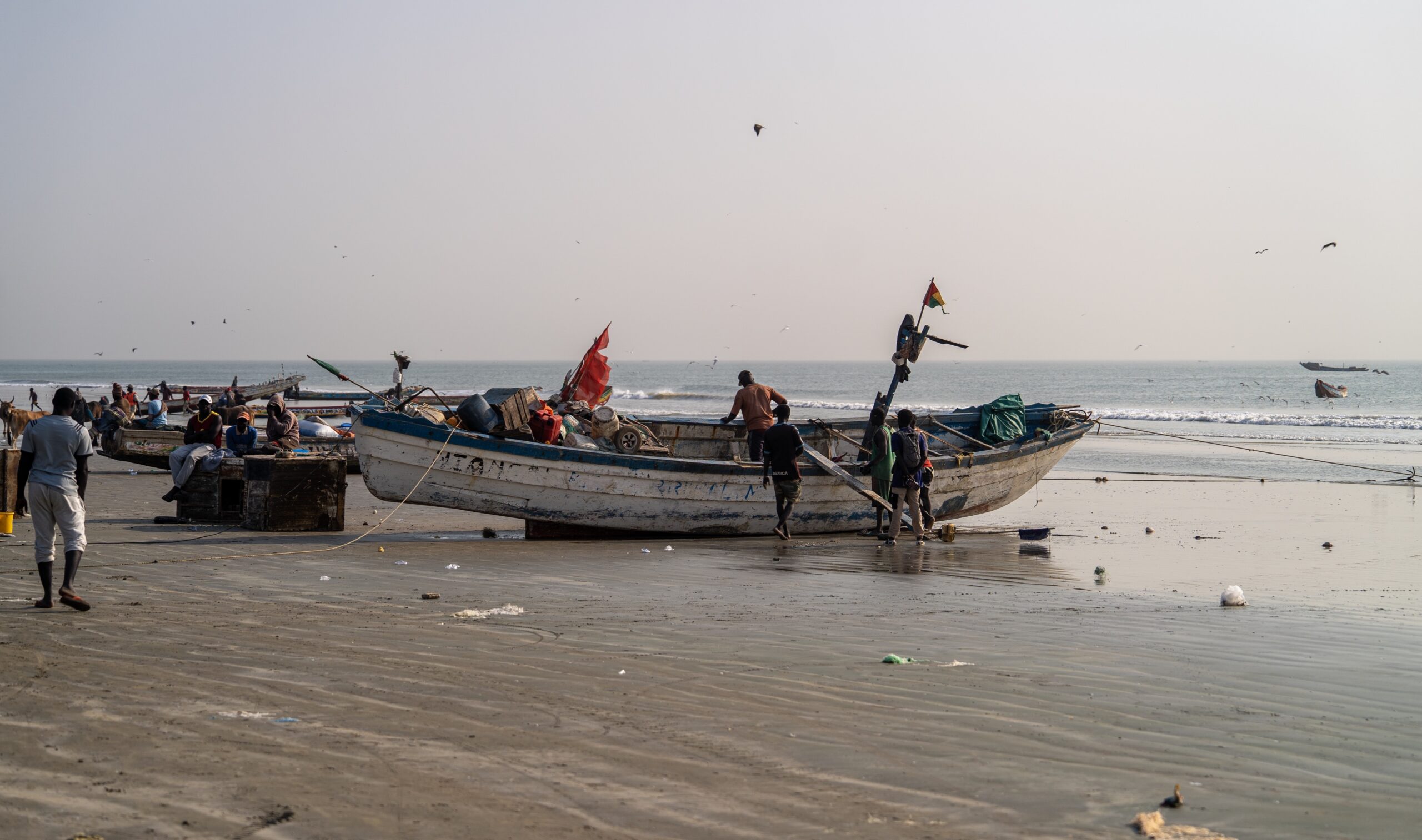 People and fishing boats on a beach with sea in background.